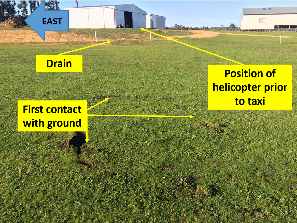 Figure 1: Marks where the helicopter tail and skid struck the ground. The drain the pilot planned to clear prior to transitioning to forward flight and hangar arein the background